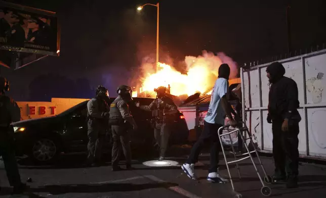 A man looks back at a fire after law enforcement helped him out of a car during a protest in Compton, Calif., Saturday, June 7, 2025, after federal immigration authorities conducted operations. (AP Photo/Ethan Swope)