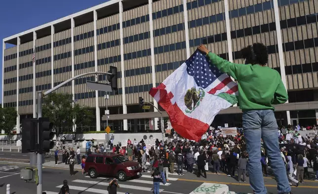 A person holds up an American and Mexican flag outside the Federal Building after federal immigration authorities conducted an operation Friday, June 6, 2025, in Los Angeles. (AP Photo/Damian Dovarganes)