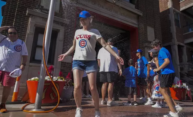 Baseball fans cool off under a sprinkler provided by the Chicago Fire Department outside of Wrigley Field after a hot baseball game between the Seattle Mariners and Chicago Cubs, Saturday, June 21, 2025, in Chicago. (AP Photo/Erin Hooley)