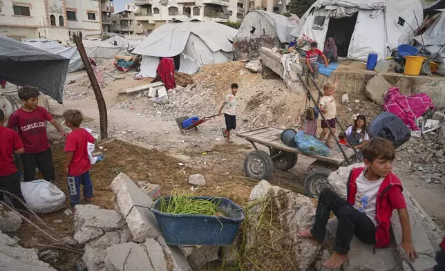 Palestinian youth and children are seen at a tent camp set up amid war-damaged infrastructure in Gaza City, Monday, June 23, 2025. (AP Photo/Jehad Alshrafi)