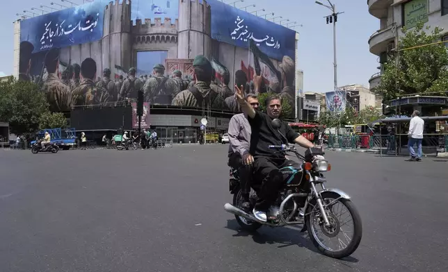 A man flashes a victory sign while riding his motorbike past an anti-Israeli banner depicting Iranian soldiers heading to attack Israeli territory, at Islamic Revolution Square in Tehran, Iran, Saturday, June 14, 2025. (AP Photo/Vahid Salemi)