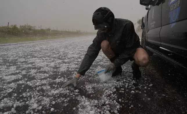 Tony Illenden crouches in a helmet and gloves outside Northern Illinois University's Husky Hail Hunter vehicle to scoop hail into a bag during a storm while on a Project ICECHIP operation Friday, June 6, 2025, in Levelland, Texas. (AP Photo/Carolyn Kaster)