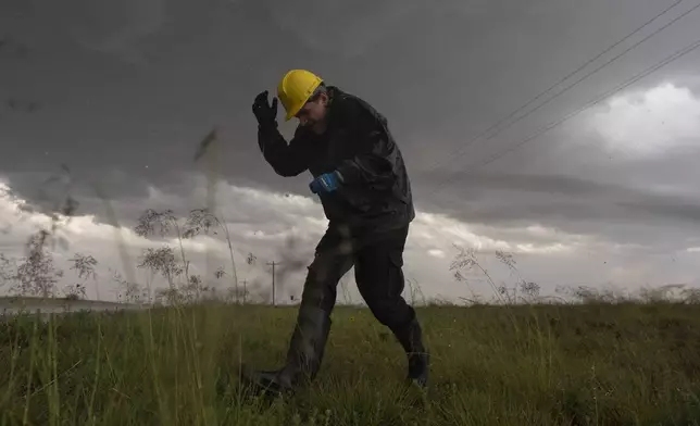 Joey Toniolo ducks from falling hail as he moves back to Northern Illinois University's Husky Hail Hunter vehicle during a Project ICECHIP operation Friday, June 6, 2025, in Morton, Texas. (AP Photo/Carolyn Kaster)