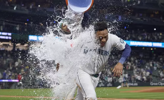 Seattle Mariners' Jorge Polanco is doused with water by J.P. Crawford after his walk off single against Cleveland Guardians during the ninth inning of a baseball game, Saturday, June 14, 2025, in Seattle. (AP Photo/John Froschauer)
