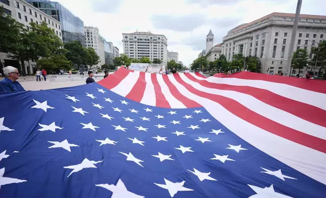 People hold a large American flag at Freedom Plaza before a parade commemorating the Army's 250th anniversary, coinciding with President Donald Trump's 79th birthday, Saturday, June 14, 2025, in Washington. (AP Photo/Manuel Balce Ceneta)