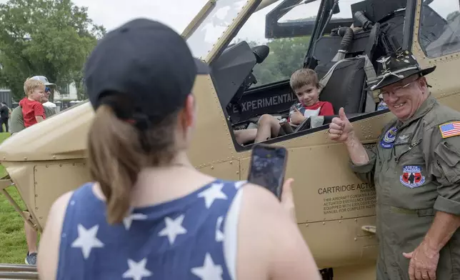 Retired Army CW4 Floyd Werner Jr., right, poses with Victor Koza, 5, center, as his mother, Melinda Koza, left, takes a photo in front of an AH-1F Cobra 998 helicopter during an event to honor the Army's 250th anniversary, coinciding with President Donald Trump's 79th birthday, Saturday, June 14, 2025, in Washington. (AP Photo/Rod Lamkey, Jr.)