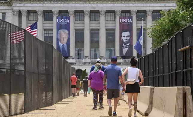 People walk in between security fencing and concrete barricades toward a large photograph of President Donald Trump and President Abraham Lincoln, draped on the USDA building, Friday, June 13, 2025, on the National Mall in Washington. (AP Photo/Jacquelyn Martin)
