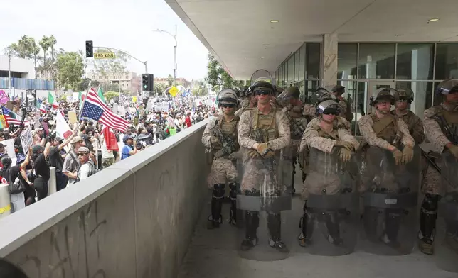 U.S. Marines guard a federal building as protesters stand outside on Saturday, June 14, 2025, in Los Angeles. (AP Photo/Ethan Swope)