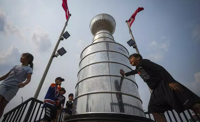 Kids from Pierceland, Saskatchewan, in the city on vacation, stop to touch and look at a nearly 4 meter replica of the Stanley Cup trophy, Tuesday, June 3, 2025, that is a permanent installation in Edmonton, Alberta, ahead of Game 1 of the NHL hockey Stanley Cup final series between the Florida Panthers the Edmonton Oilers. (Darryl Dyck/The Canadian Press via AP)