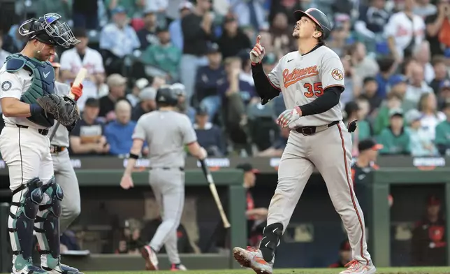 Baltimore Orioles' Adley Rutschman (35) celebrates at home plate after hitting a solo home run as Seattle Mariners catcher Mitch Garver looks on during the sixth inning of a baseball game, Wednesday, June 4, 2025, in Seattle. (AP Photo/Jason Redmond)
