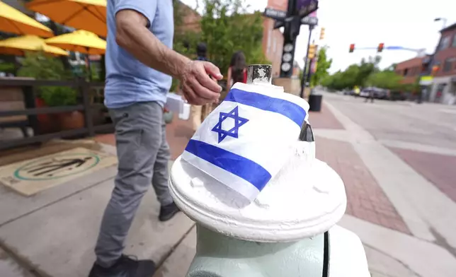 A passer-by touches the flag of Israel taped on to the top of a bollard on the east end of the Pearl Street Mall near the Boulder County, Colo., courthouse Monday, June 2, 2025, in Boulder, Colo. (AP Photo/David Zalubowski)