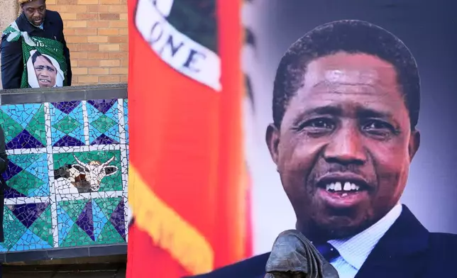 A supporter arrives for a Mass for former Zambian President Edgar Lungu, shown in a banner at right, at the Cathedral of Christ the King in Johannesburg, South Africa, Wednesday, June 25, 2025. (AP Photo/Themba Hadebe)