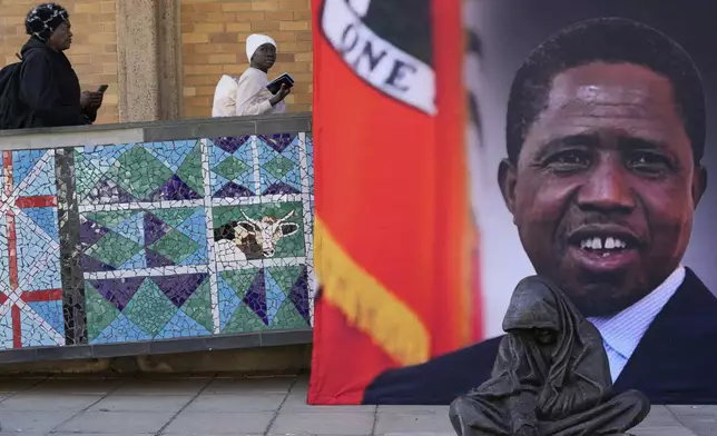 Mourners arrive to attend a Mass for former Zambian President Edgar Lungu, shown in a banner at right, at the Cathedral of Christ the King in Johannesburg, South Africa, Wednesday, June 25, 2025. (AP Photo/Themba Hadebe)