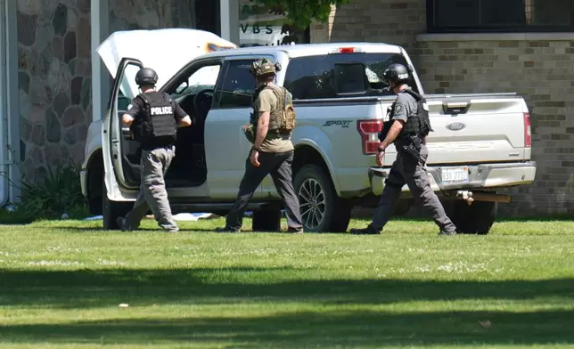 Police walk by an idle vehicle near CrossPointe Community Church in Wayne, Mich., Sunday, June 23, 2025. (AP Photo/Paul Sancya)