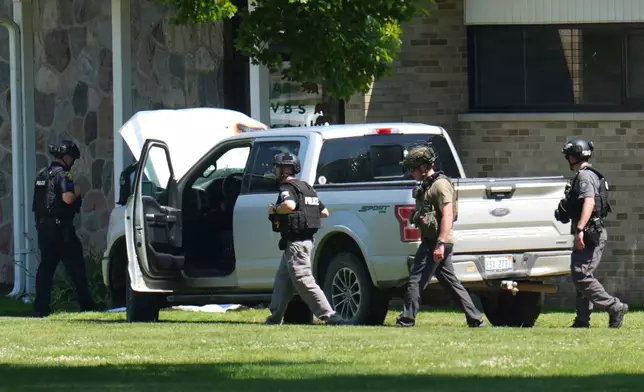 Police walk by an idle vehicle near CrossPointe Community Church in Wayne, Mich., Sunday, June 23, 2025. (AP Photo/Paul Sancya)