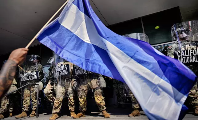 A protester waves a national flag from El Salvador in front of a line of California National Guard guarding the front of a federal building in downtown Los Angeles on Monday, June 9, 2025. (AP Photo/Eric Thayer)