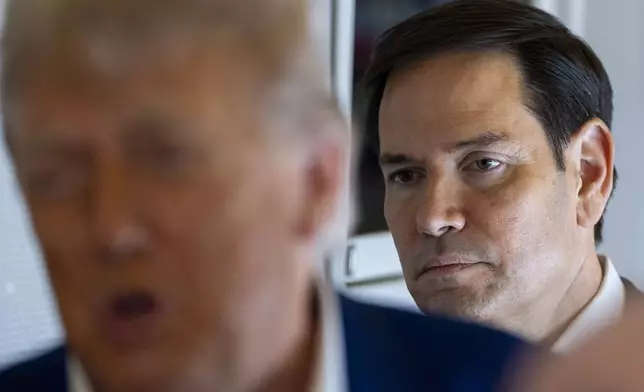 Secretary of State Marco Rubio stands behind as President Donald Trump speaks with reporters on Air Force One while in flight from Joint Base Andrews, Md., to Amsterdam, Netherlands, Tuesday, June 24, 2025. (AP Photo/Alex Brandon)