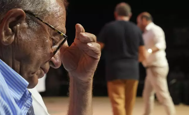 A judge lifts his hand to his head as Cypriot lyricists Savvas Demetriou, 46, rear left, and Constantinos Christou Girlias, 44, battle it out live on stage in the centuries-old duel known as "tsiattista" at the Pentecost Festival in Cyprus' southern coastal town of Larnaca, Sunday, June 8, 2025. (AP Photo/Petros Karadjias)