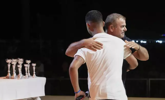 Cypriot lyricists Savvas Demetriou, 46, rear, and Rafael Georgiou, 17, embrace after battling it out live on stage in the centuries-old duels known as "tsiattista" at the Pentecost Festival in Cyprus' southern coastal town of Larnaca, Sunday, June 8, 2025. (AP Photo/Petros Karadjias)