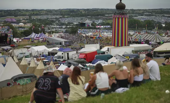 Festivalgoers sit outside a bar during the Glastonbury Festival in Worthy Farm, Somerset, England, Wednesday, June 25, 2025. (Scott A Garfitt/Invision/AP)