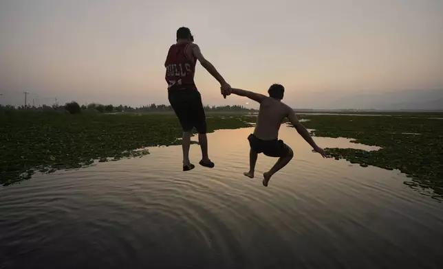 Boys jump together as they cool off on a hot summer day at Dal Lake in Srinagar, Indian-controlled Kashmir, Monday, June 23, 2025. (AP Photo/Mukhtar Khan)