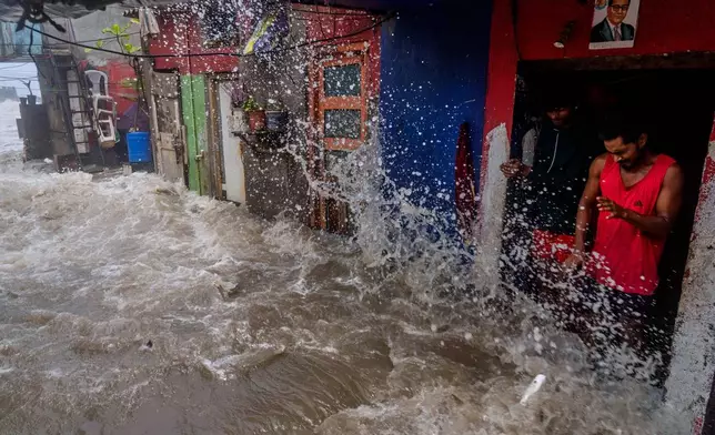 Men watch as waves hit houses during high tide on the shore of the Arabian Sea in Mumbai, India, Wednesday, June 25, 2025. (AP Photo/Rafiq Maqbool)