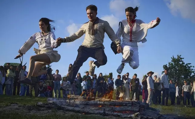 People jump over bonfire during a traditional midsummer celebration in Pyrohiv, Ukraine, outside of Kyiv, Saturday, June 21, 2025. (AP Photo/Efrem Lukatsky)