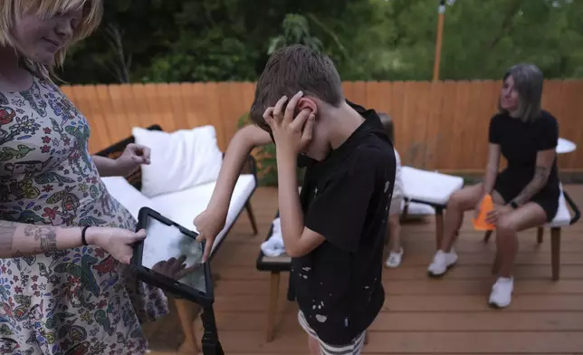 Charlie Lamb, who is diagnosed with autism and is non-verbal, uses an AAC device to communicate with a caregiver, Monday, May 12, 2025, in Austin, Texas. (AP Photo/Eric Gay)