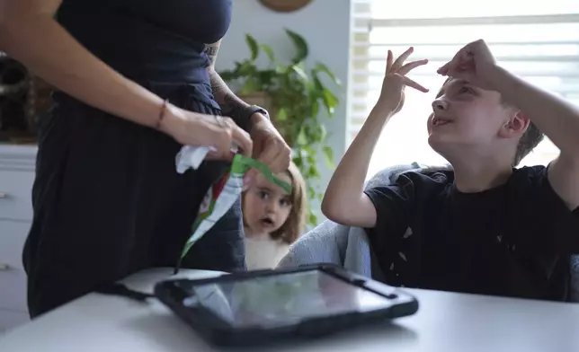 Charlie Lamb, right, who is diagnosed with autism and is non-verbal, uses an AAC device to communicate with his mother Eileen Lamb left, who also has autism, as Charlie's sister Billie looks on, Monday, May 12, 2025, in Austin, Texas. (AP Photo/Eric Gay)