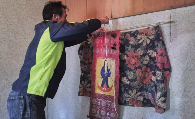Masatsugu Tanimoto, a farmer and one of the few remaining hidden Christians on Ikitsuki Island, hangs a scroll of the Virgin Mary and Jesus once secretly worshipped at his home in Ikitsuki Island in Hirado, southern Japan, Sunday, April 27, 2025. (AP Photo/Eugene Hoshiko)