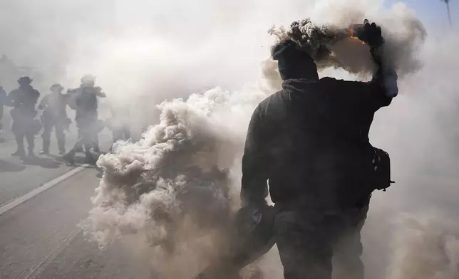 A protester throws a smoke canister on the 101 Freeway near the metropolitan detention center of downtown Los Angeles, Sunday, June 8, 2025, following last night's immigration raid protest. (AP Photo/Eric Thayer)