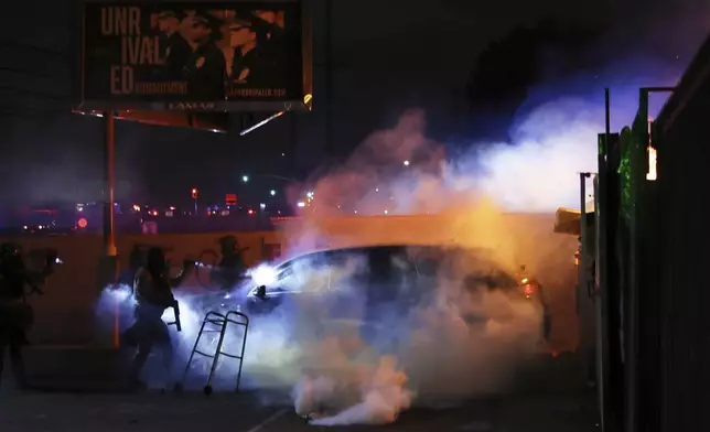 Law enforcement investigate a car with a person inside during a protest in Compton, Calif., Saturday, June 7, 2025, after federal immigration authorities conducted operations. (AP Photo/Ethan Swope)