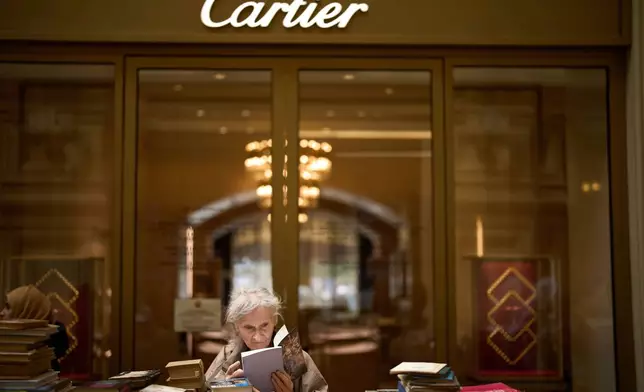 A woman reads a book while standing at a book shop next to a Cartier boutique, that was closed due to sanctions, at the GUM Department store during the annual Red Square Book Festival, celebrating Alexander Pushkin's birthday with days of free concerts, readings, lectures and kids' events in Red Square in Moscow, Russia, Wednesday, June 4, 2025. (AP Photo/Alexander Zemlianichenko)