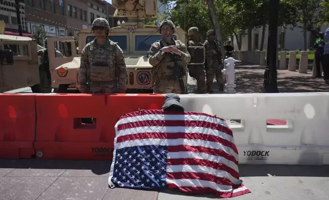 Protester Annie Jones holds a U.S. Flag upside down as a sign of distress while California National Guard stand behind a barricade in Santa Ana, Calif. on Tuesday, June 10, 2025. (AP Photo Jae C. Hong)