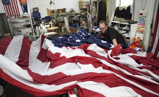 Tim O'Connor, back left, and his son Matthew O'Connor, work on a large United States flag at Humphrys Flag Company that will be draped outside their building for Flag Day, in Philadelphia, Tuesday, June 10, 2025. (AP Photo/Matt Rourke)