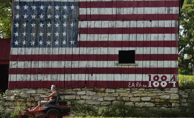 Karrie Brewer mows in front of a flag-painted barn Saturday, June 7, 2025, on the family farm near Loring, Kan. The barn was painted by her husband, Quentin Brewer, who's birthday is flag day, with 38 stars representing the number of states in the union when the barn was built in 1884. (AP Photo/Charlie Riedel)