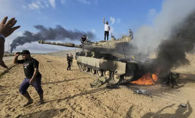 FILE - Palestinians celebrate by a destroyed Israeli tank at the border fence between Israel and the Gaza Strip, east of Khan Younis, during a surprise attack on Israel, Saturday, Oct. 7, 2023. (AP Photo, File)