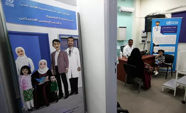A doctor consults with a woman and her child at a medical center run by UNRWA in the Mar Elias refugee camp in Beirut, Lebanon, Monday, June 2, 2025. Posters in Arabic promote UNRWA's mental health and medical services for Palestinian refugees. (AP Photo/Hassan Ammar)