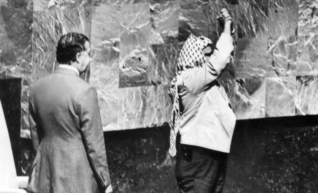 FILE - A holster protrudes from under Yasser Arafat's jacket as he clasps his hands over his head during his appearance before the United Nations General Assembly at the U.N. headquarters, Nov. 13, 1974. (AP Photo, File)