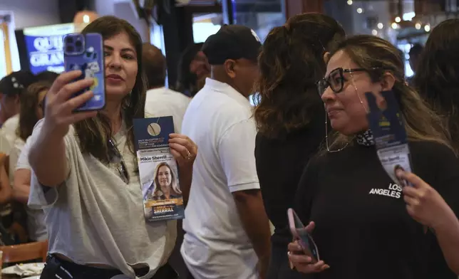 Attendees pose for photos holding a campaign pamphlet of Rep. Mikie Sherrill, D-N.J., during a "Get Out the Vote" rally, Saturday, June 7, 2025, in Elizabeth, N.J. (AP Photo/Heather Khalifa)