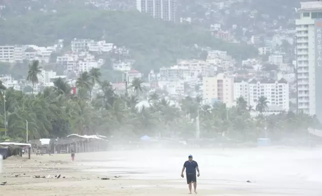 A tourist walks on Manzanillo beach as Hurricane Erick passes near Acapulco, Mexico, Thursday, June 19, 2025. (AP Photo/Fernando Llano)