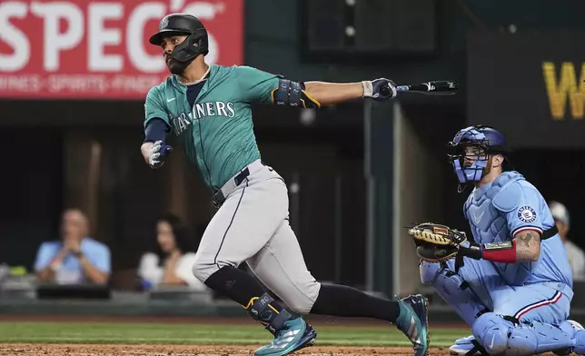 Seattle Mariners' Julio Rodriguez follows through on a single as Texas Rangers catcher Jonah Heim, right, looks on in the third inning of a baseball game, Sunday, June 29, 2025, in Arlington, Texas. (AP Photo/Tony Gutierrez)