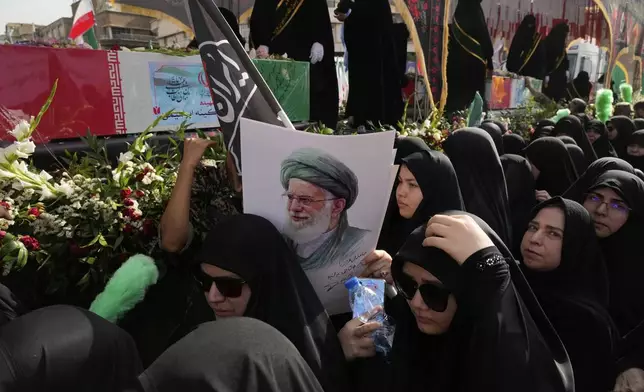 Mourners gather around the flag-draped coffins of the Iranian armed forces generals, nuclear scientists and their family members who were killed in Israeli strikes, during their funeral ceremony as one of them holds a poster of the Supreme Leader Ayatollah Ali Khamenei, in Tehran, Iran, Saturday, June 28, 2025. (AP Photo/Vahid Salemi)