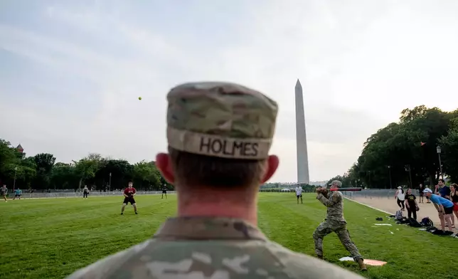 Seen through security fencing, Army Spc. Steven Holmes, left, watches Army Sgt. Chase Beasley, right, take a swing as they sit-in on a game of softball with congressional staffers on the National Mall, during preparations for an upcoming military parade commemorating the Army's 250th anniversary and coinciding with President Donald Trump's 79th birthday, Thursday, June 12, 2025, in Washington. (AP Photo/Rod Lamkey, Jr.)