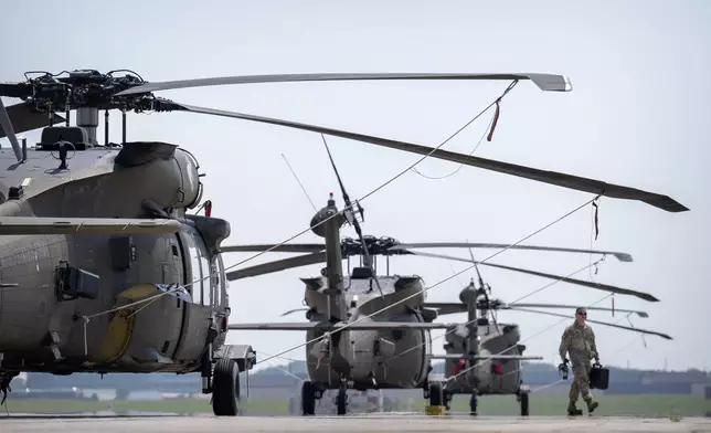 A crew member walks past U.S. Army UH-60M Black Hawk helicopters that will participate in an upcoming military parade commemorating the Army's 250th anniversary and coinciding with President Donald Trump's 79th birthday, at Joint Base Andrews, Md., Thursday, June 12, 2025. (AP Photo/Mark Schiefelbein)