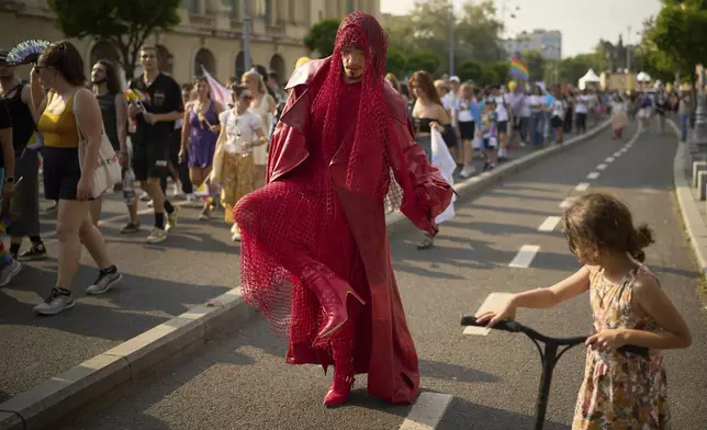 A child pauses to look at a participant adjusting his outfit in the Bucharest Pride Parade in Bucharest, Romania, Saturday, June 7, 2025. (AP Photo/Vadim Ghirda)