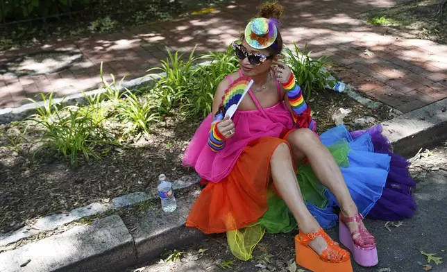 A person dressed in rainbow colors fans themselves while sitting on a curb before the World Pride parade, Saturday, June 7, 2025, in Washington. (AP Photo/Julia Demaree Nikhinson)