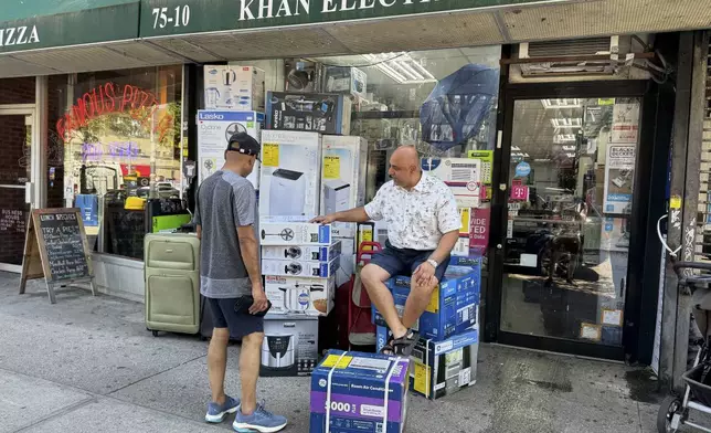 Mudassar Khan, right, talks with a customer while sitting outside his electronics store with air conditioners and fans for sale on display, Tuesday, June 24, 2025, in New York. (AP Photo/Cedar Attanasio)