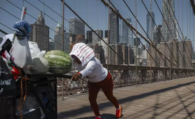 A fruit vendor pushes her cart on the Brooklyn Bridge during a heatwave on Tuesday, June 24, 2025, in New York. (AP Photo/Olga Fedorova)