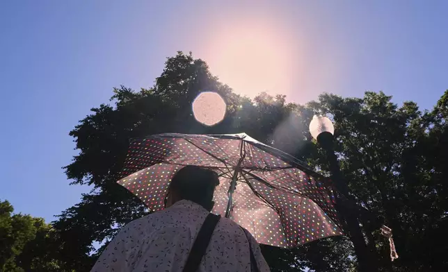 With temperatures hovering near 100 degrees, a woman protects herself from the sun while walking through Boston Common, Tuesday, June 24, 2025, in Boston. (AP Photo/Charles Krupa)